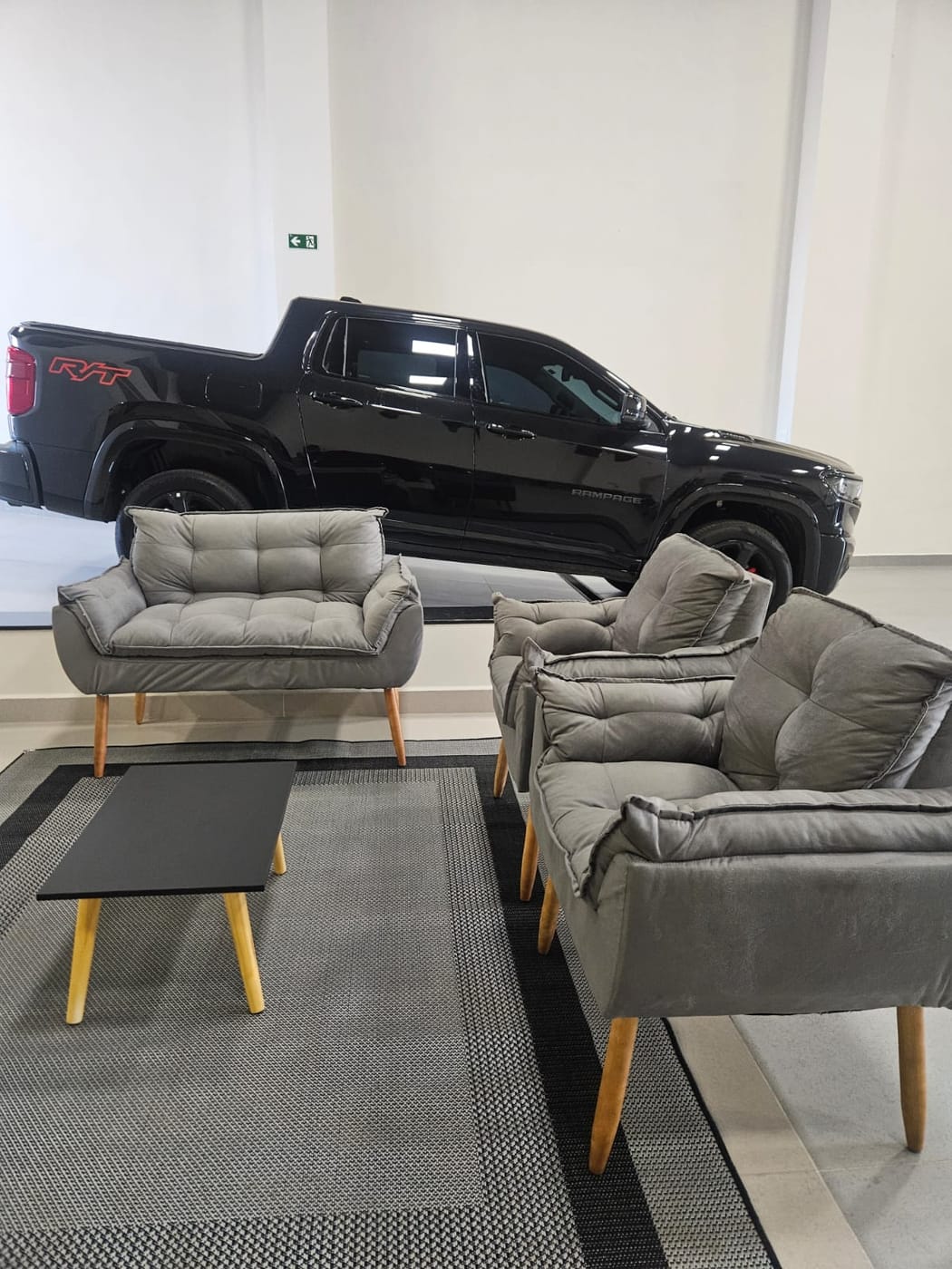 Picape RAM Rampage R/T preta sobre o palanque de exposição, atrás das poltronas cinza do lounge